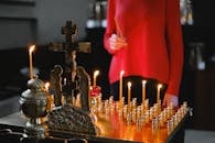 A woman lighting candles at an Orthodox altar with cross and statues in a church.